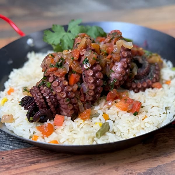 Grilled octopus with pico de gallo and cilantro, served over rice with vegetables in a pan.